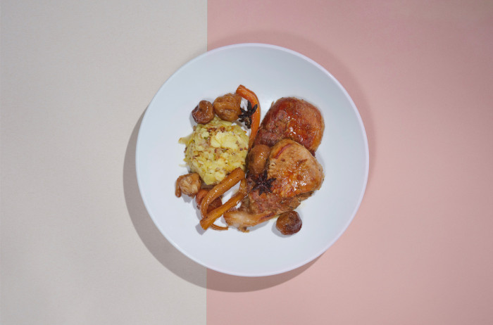 A white plate on a beige and pink base. Neatly arranged slices of roast, potatoes, and fig slices on the plate.