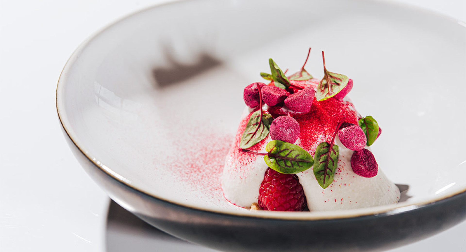  A white mousse on a deep plate, garnished with raspberries and green leaves. White background.
