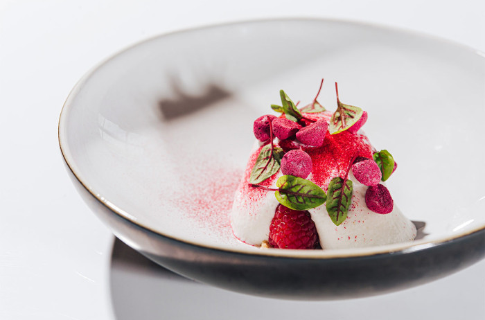  A white mousse on a deep plate, garnished with raspberries and green leaves. White background.