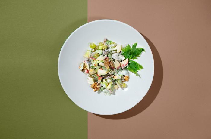  A white plate on an olive green and pink base. On the plate, a nicely presented salad with dressing, decorated with walnuts and parsley leaves.