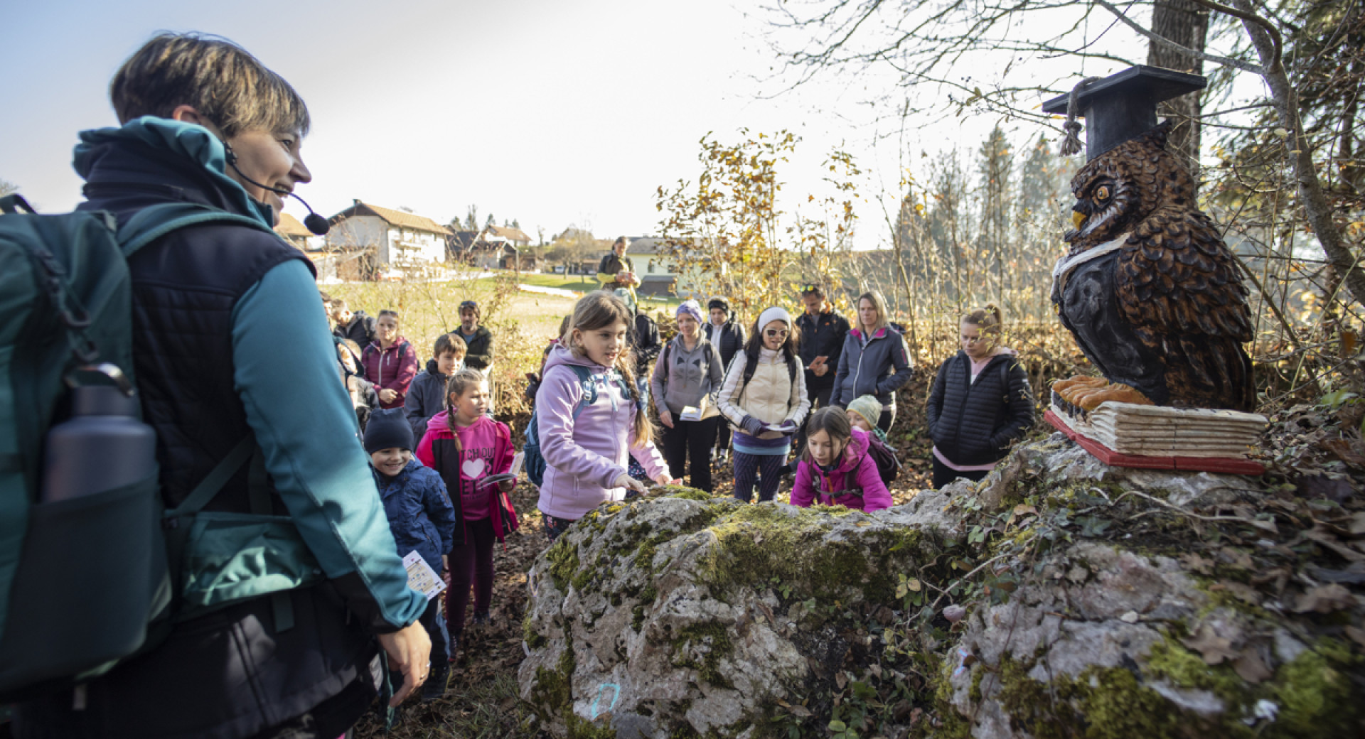 Otroci, zbrani na prostem, pred skulpturo sove na skali.