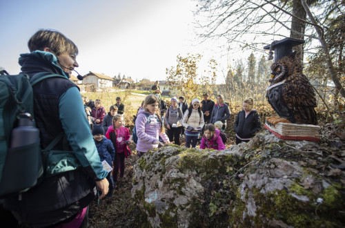 Otroci, zbrani na prostem, pred skulpturo sove na skali.