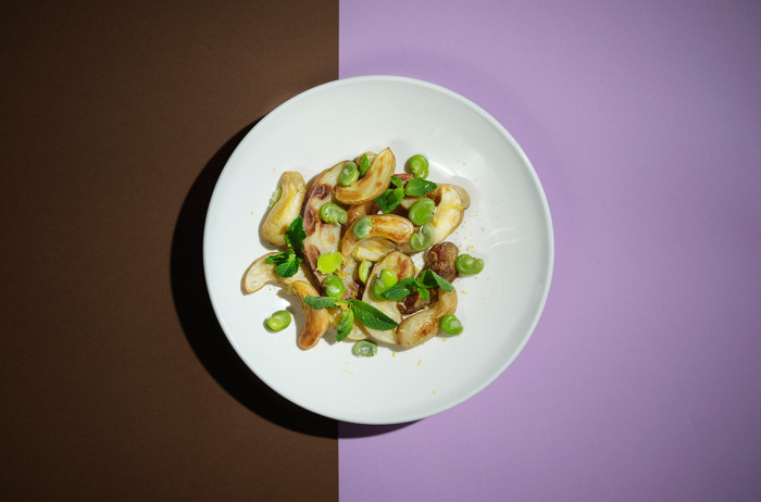 A white plate on a brown and violet base. On the plate, there's roasted potatoes sprinkled with green peas.