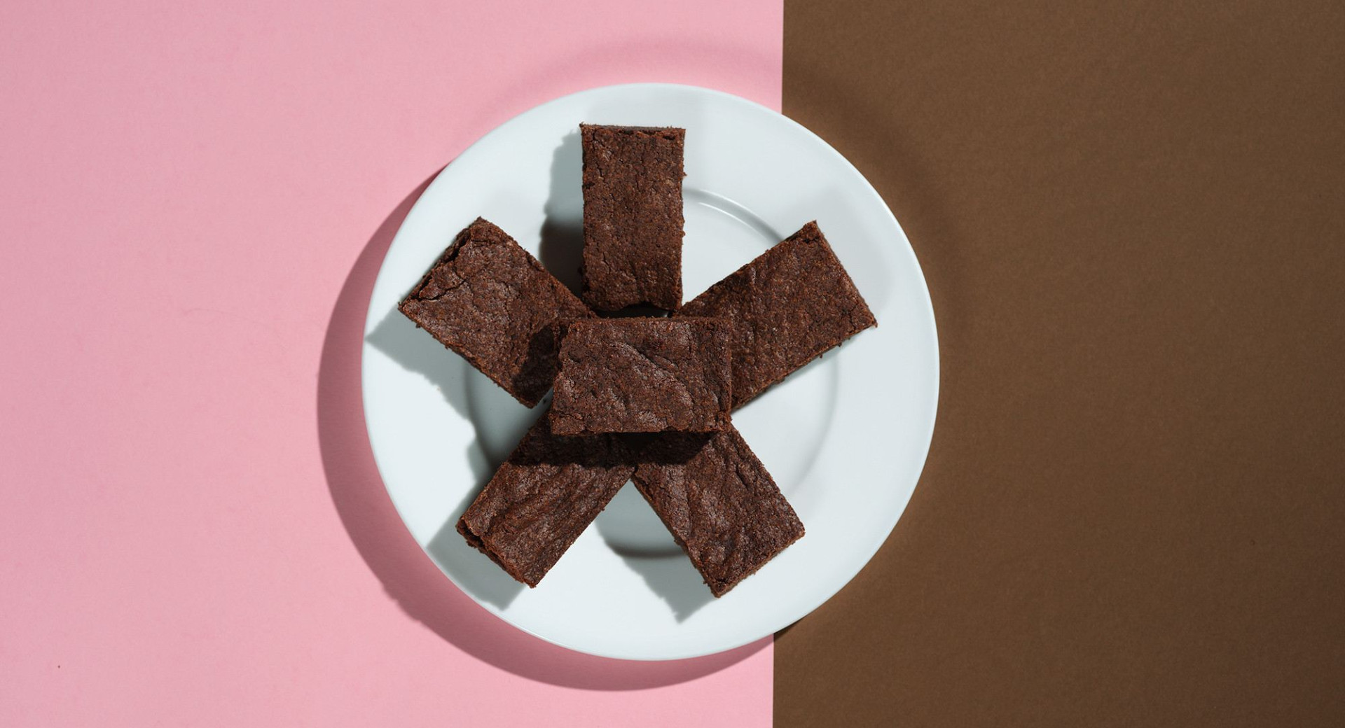 A white plate on a pink and brown base. Chocolate cubes are arranged in a star shape on the plate.