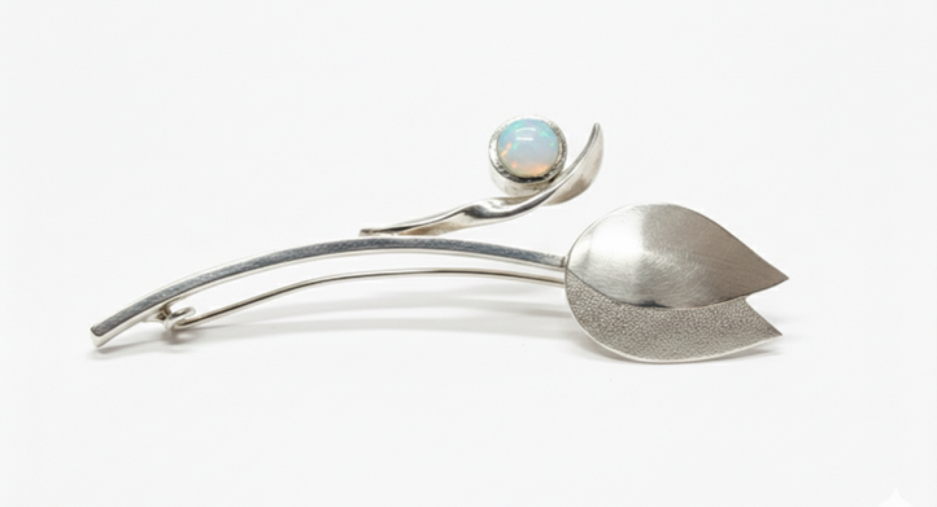 Silver jewellery in the shape of a leaf and a flower with a coloured gemstone.