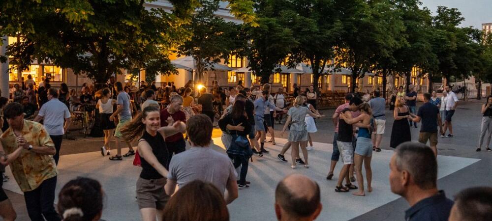 People are dancing outdoors beneath a tree-lined avenue at dusk in a warm and inviting atmosphere.