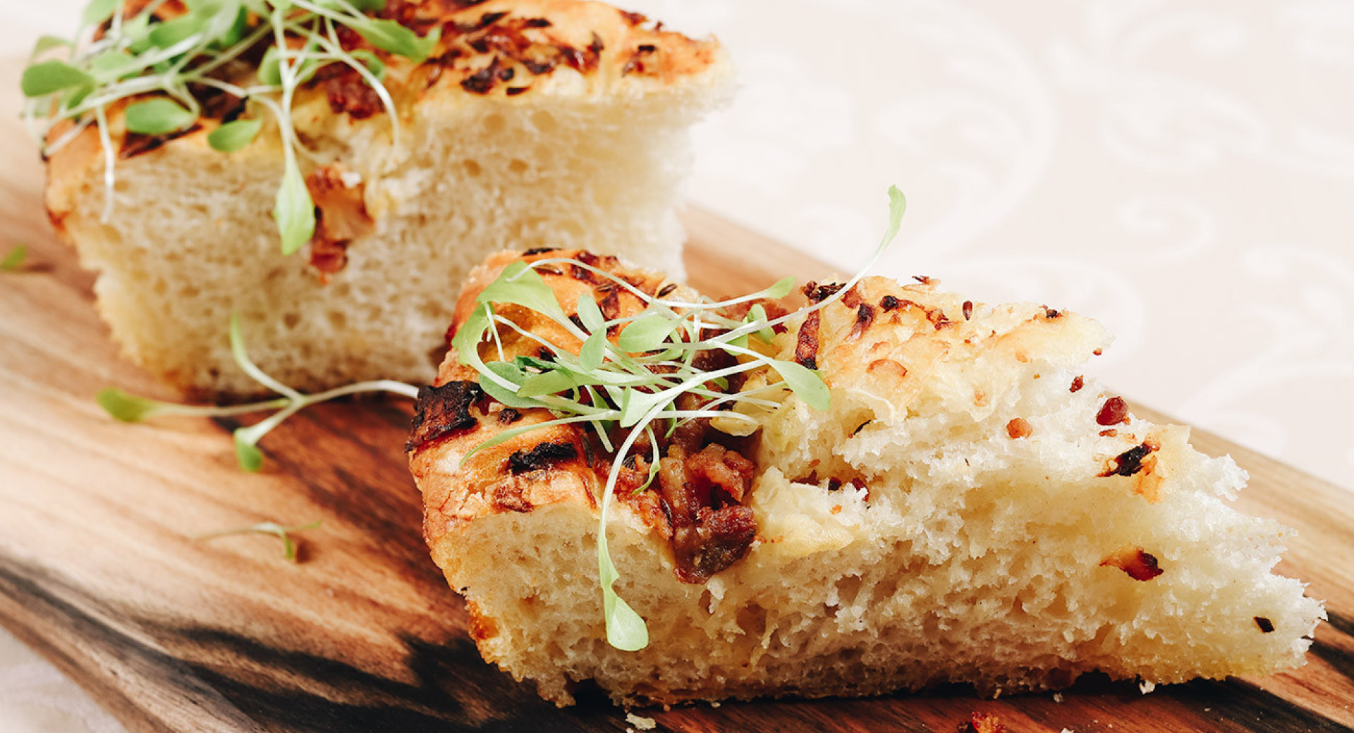 Two pieces of pogaca on a wooden board, garnished with fresh herbs.