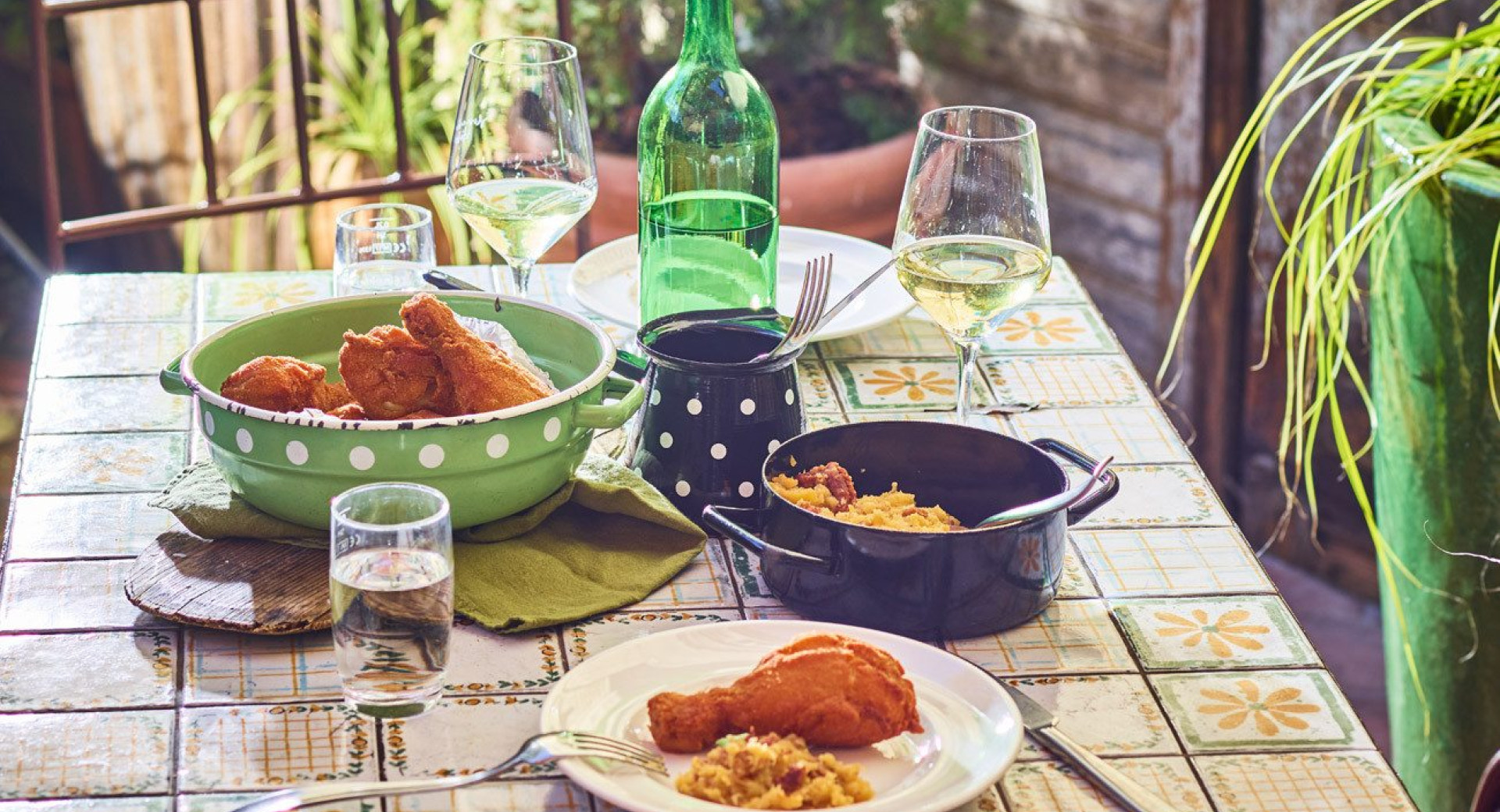 A set table in a rustic, homemade style. A beverage and flying dumplings with a side dish are served on the table. In the background, there are plants.