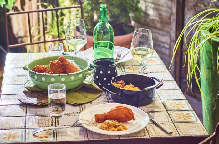 A set table in a rustic, homemade style. A beverage and flying dumplings with a side dish are served on the table. In the background, there are plants.