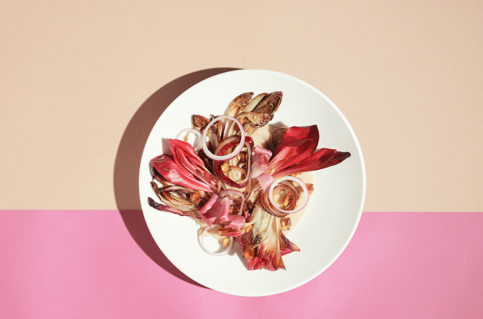  A white plate on a pink and orange background. On the plate, leaves of red radish, sprinkled with onion rings.