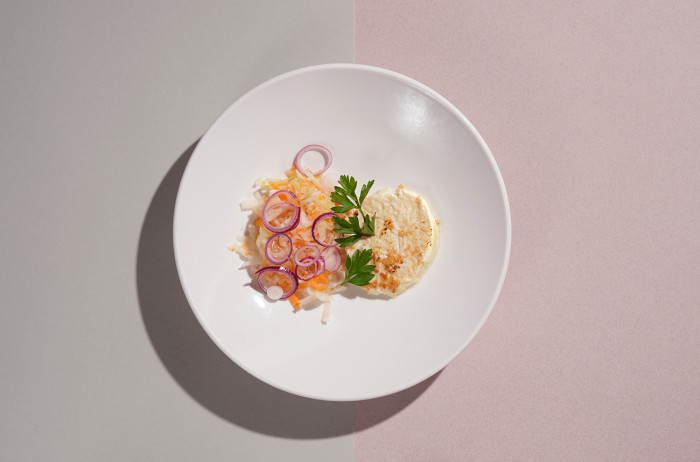 A white plate on a gray and pink base. On the plate, neatly arranged vegetables, accompanied by cheese for grilling. Decorated with parsley sprigs.