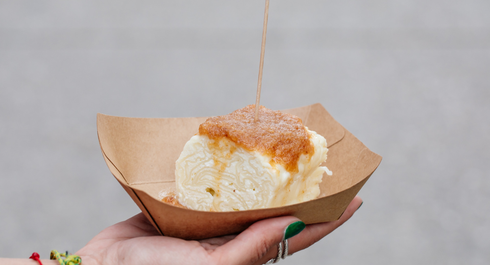 Eine Person mit grünen Fingernägeln hält einen Quarkstrukel mit Bröseln und einem Gourmet Ljubljana Fähnchen.
