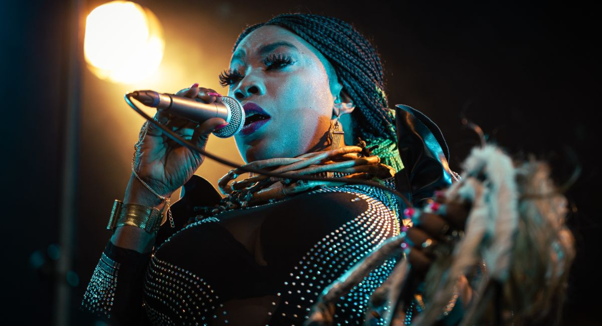 Close-up of a woman's face as she sings on stage with a microphone in her hand, a spotlight shining behind her.
