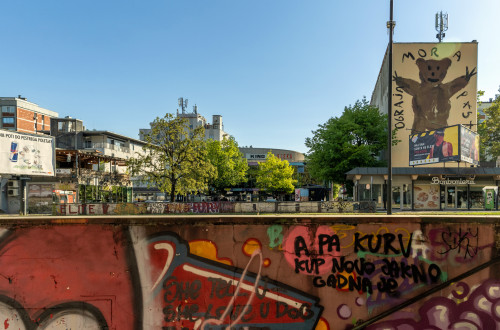 grafiti na zidu, v ozadju stavba s poslikavo medveda, drevesa