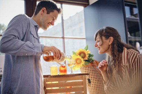 Nasmejan par; moski naliva medico v kozarec in zenska ga opazuje.