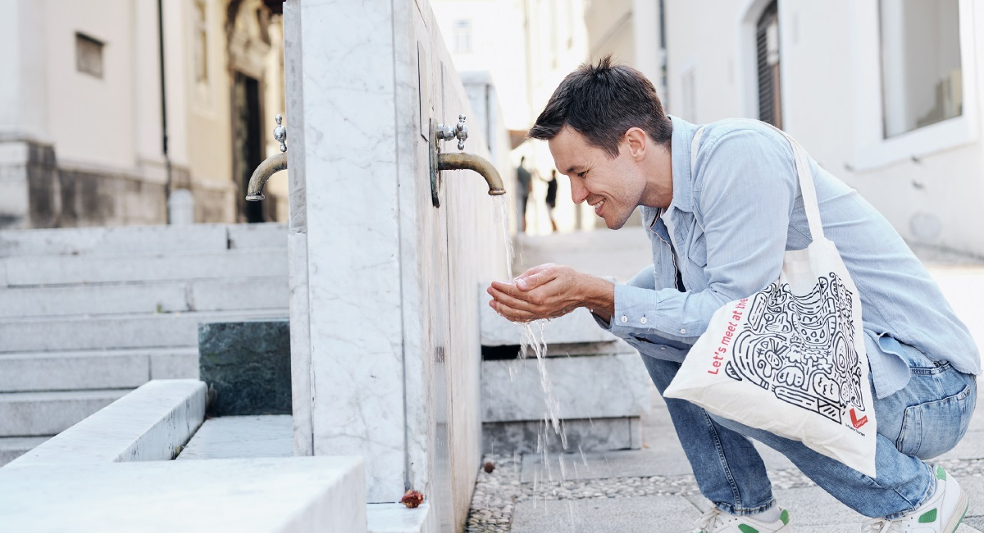 A man kneeling at a drinking fountain, drinking water.