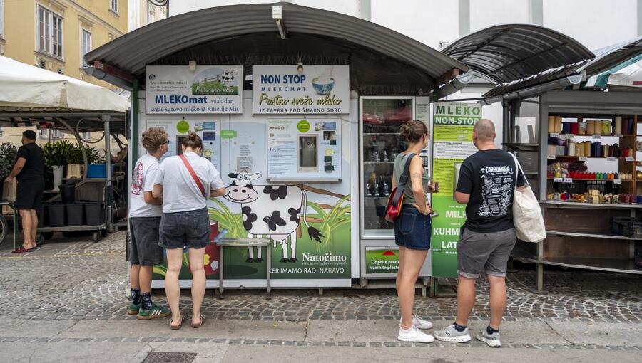 The green milk vending machine, offering fresh milk, attracts visitors who are examining the signs on the machine. It also features an illustrated cow.