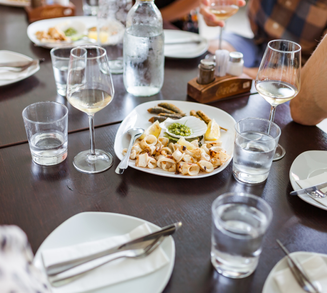 Sul tavolo bicchieri e un piatto con girice (pesciolini fritti) e calamari.
