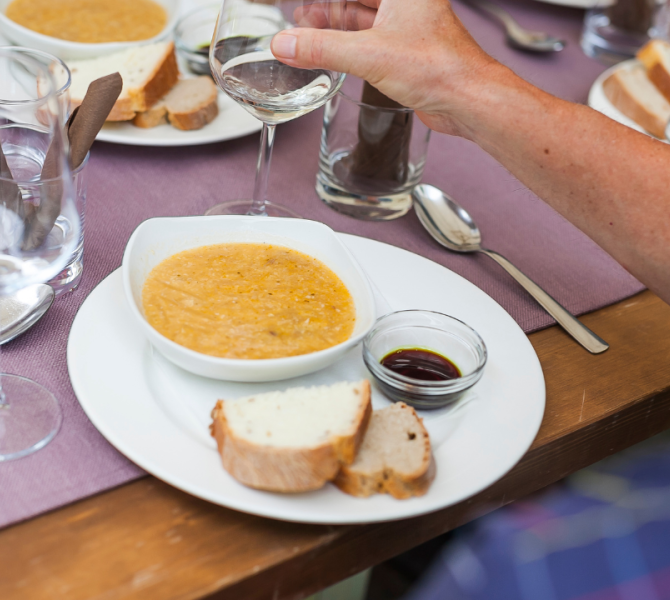 Sul tavolo un piatto di jota, con pane e olio di semi di zucca in una ciotolina a lato.