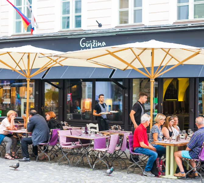 Persone sedute a un tavolo davanti a un ristorante ascoltano la spiegazione della guida.