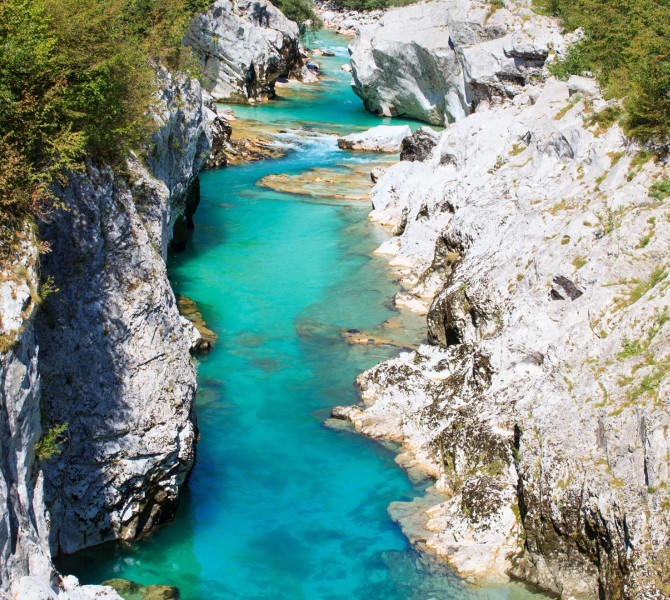Une vue en plongée d'une rivière turquoise coulant dans une gorge étroite avec des rochers de calcaire blanc et de la végétation verdoyante.