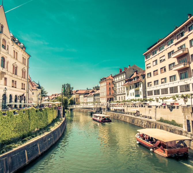 Ein Holzboot auf dem Fluss Ljubljanica, an beiden Ufern Bürgerhäuser.