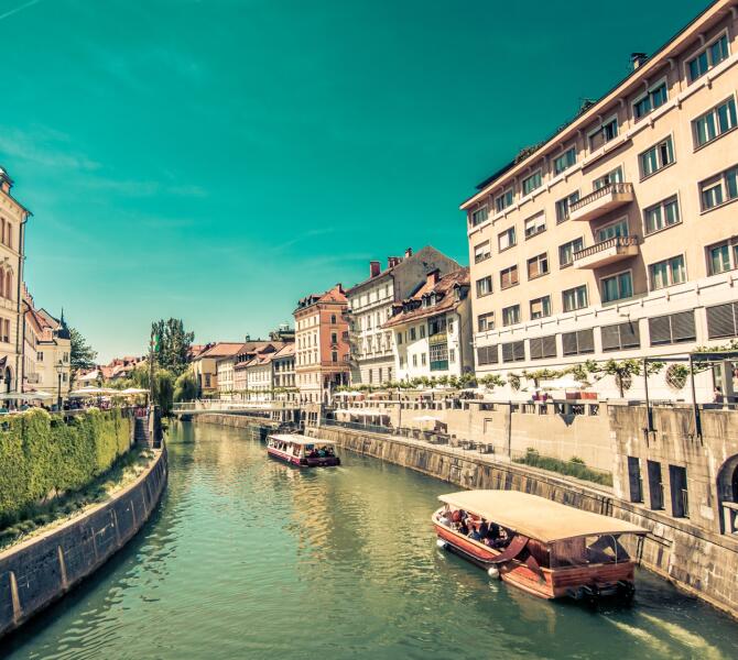 Ein Holzboot auf dem Fluss Ljubljanica, an beiden Ufern Bürgerhäuser.