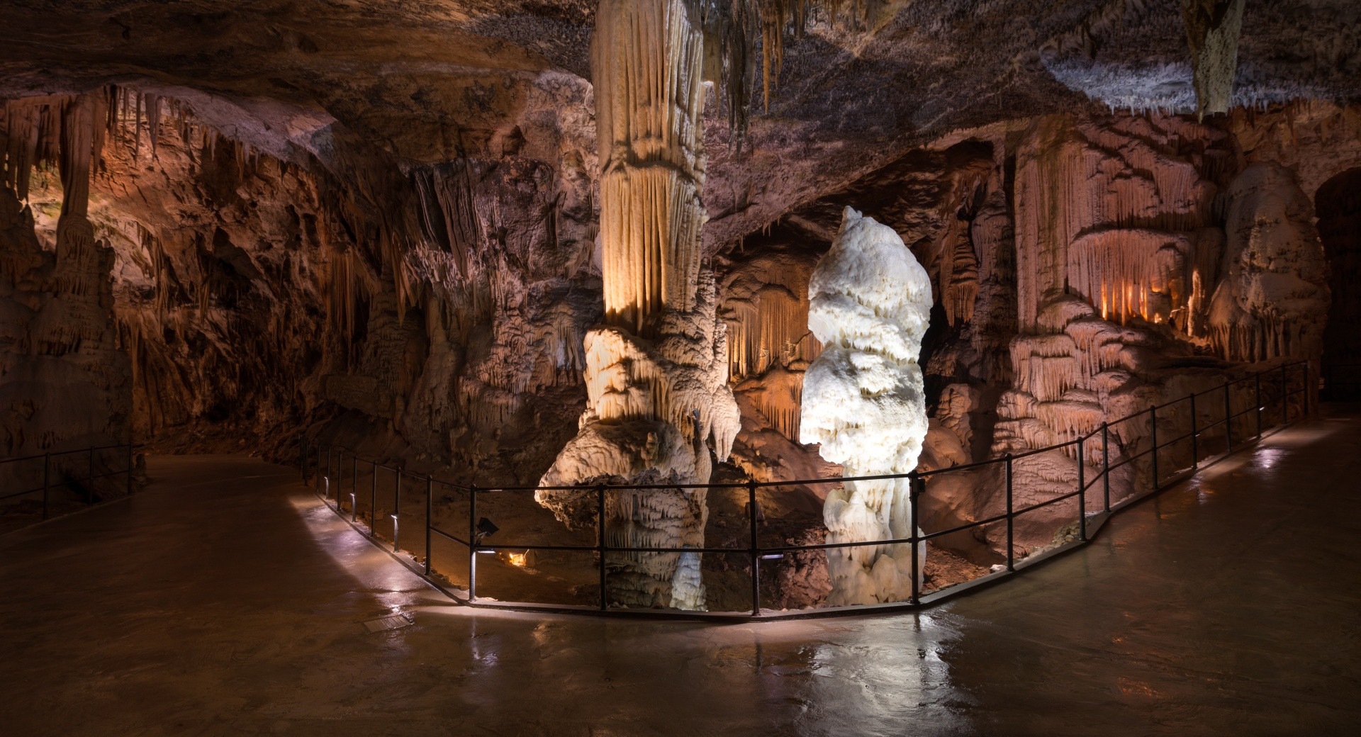 Zwei große Tropfsteine in einer Höhle, daneben ein Wanderweg.