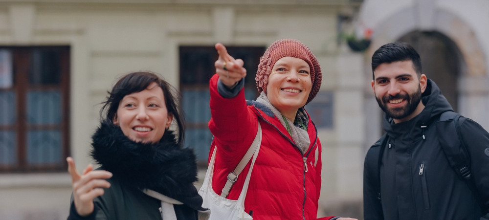 A woman in a red coat is explaining and showing something to a man and a woman beside her.