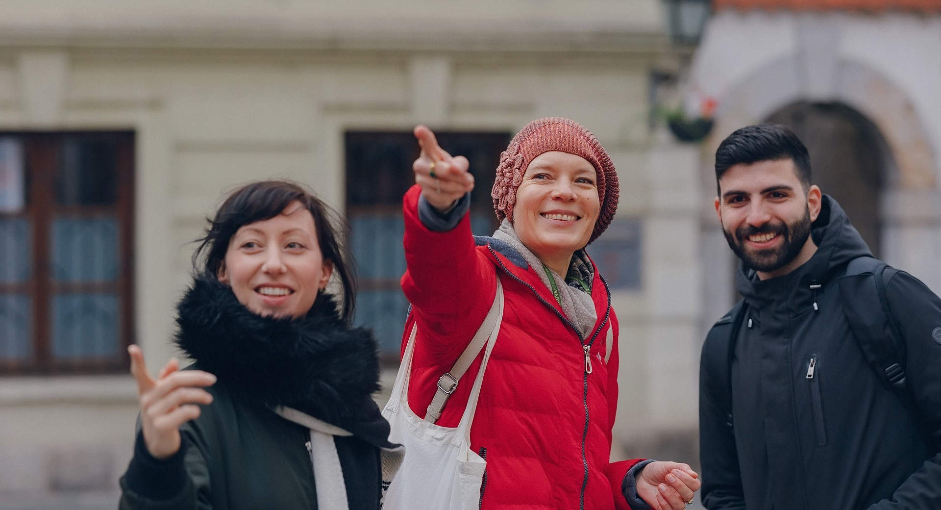 Zenska v rdeci bundi razlaga in kaze nekaj moskemu in zenski poleg sebe.