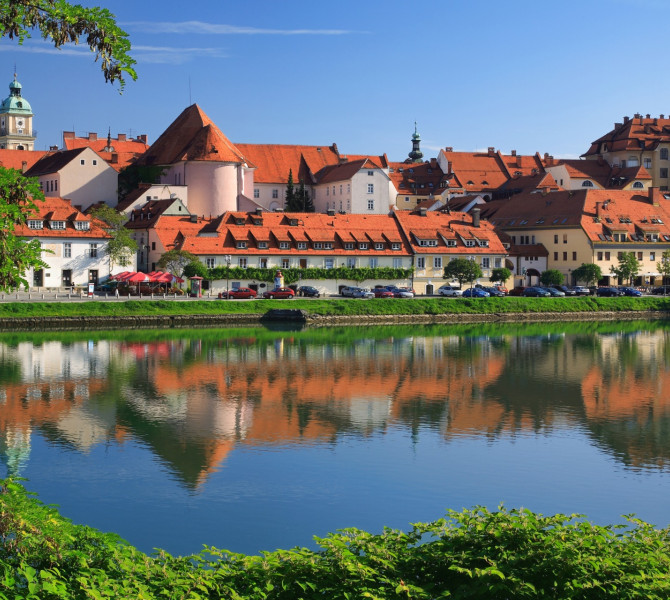 A river with greenery on the left bank and a town with bourgeois houses on the right.