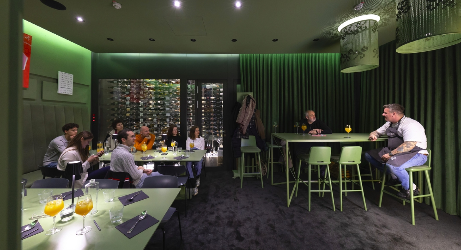 Dve osebi med pogovorom za mizo, ob njiju več ljudi, ki sedi za drugimi mizami.