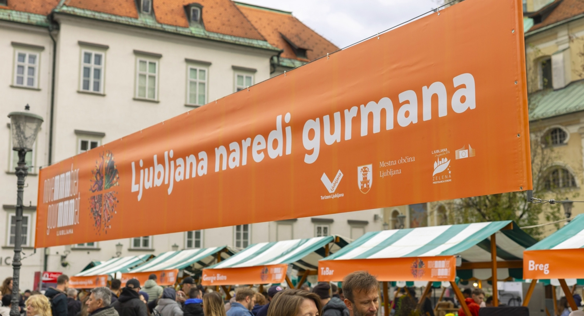 Transparent z napisom: Ljubljana naredi gurmana - nad glavami obiskovalcem na uličnem dogodku.