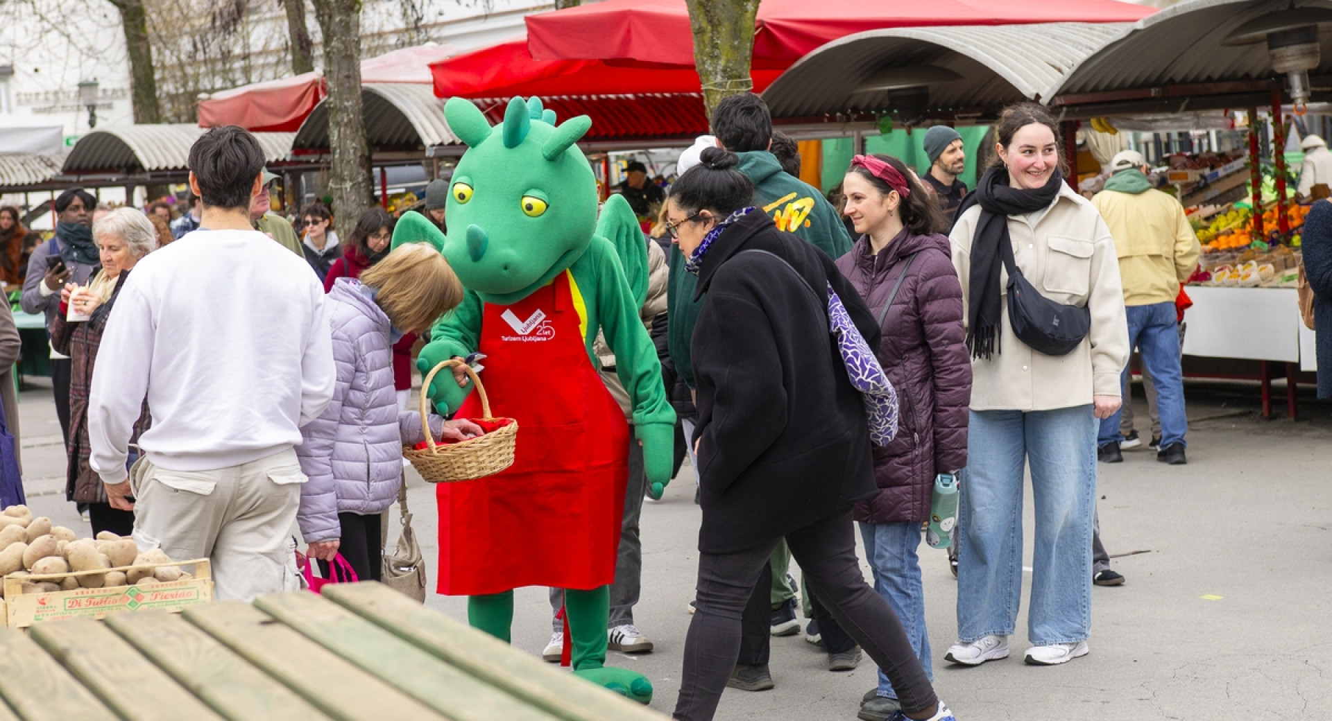 Maskota ljubljanski Zmajček deli piškote obiskovalcem na ljubljanski tržnici.