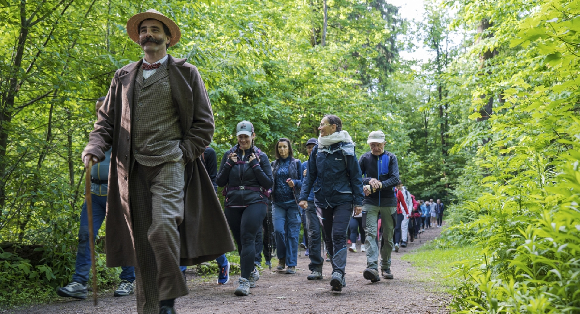 Oseba, preoblečena v pisatelja Ivana Cankarja, vodi pohodnike v naravi.