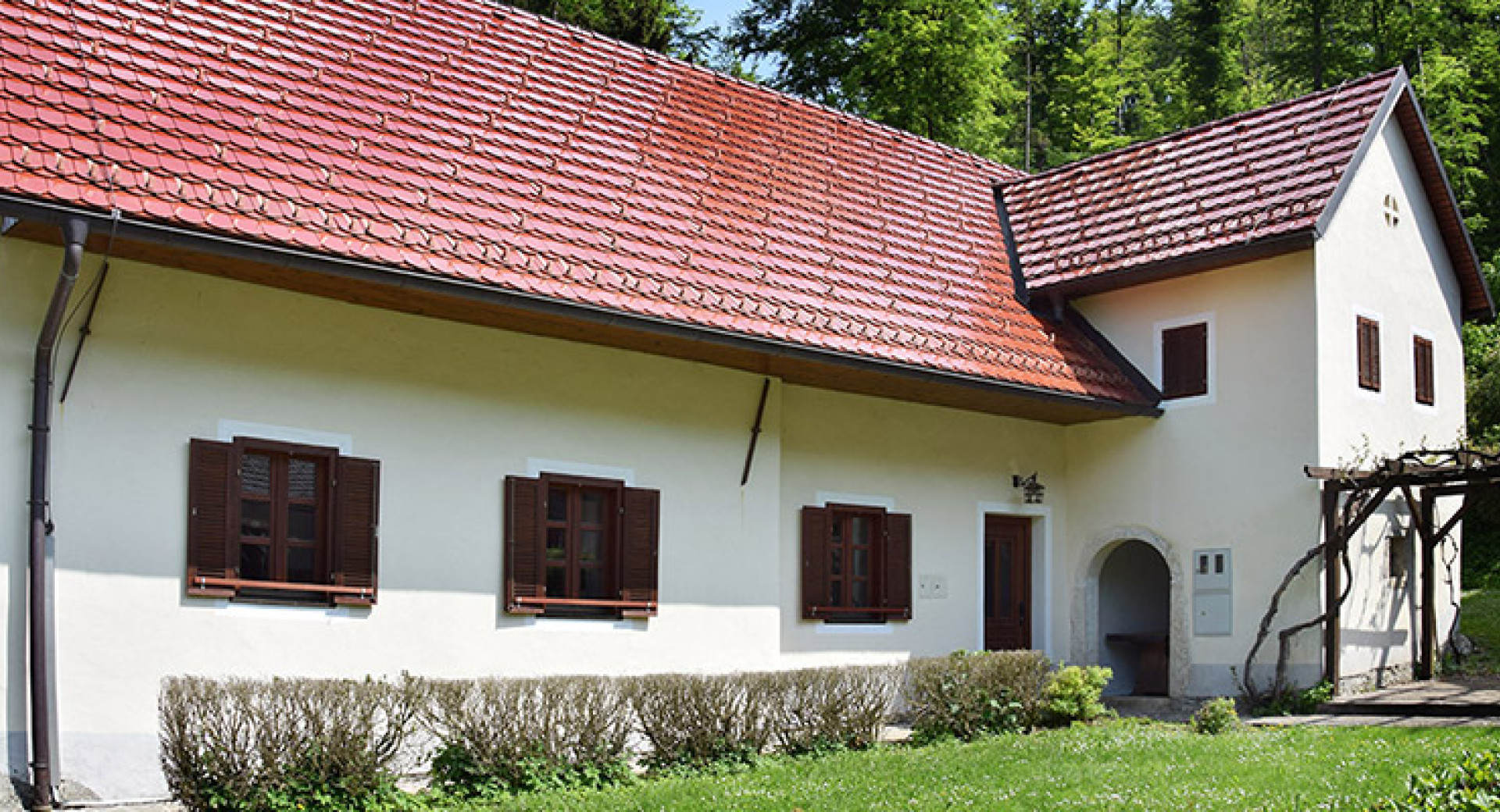 Hiša z belim pročeljem, lesenimi polknami in opečnato streho