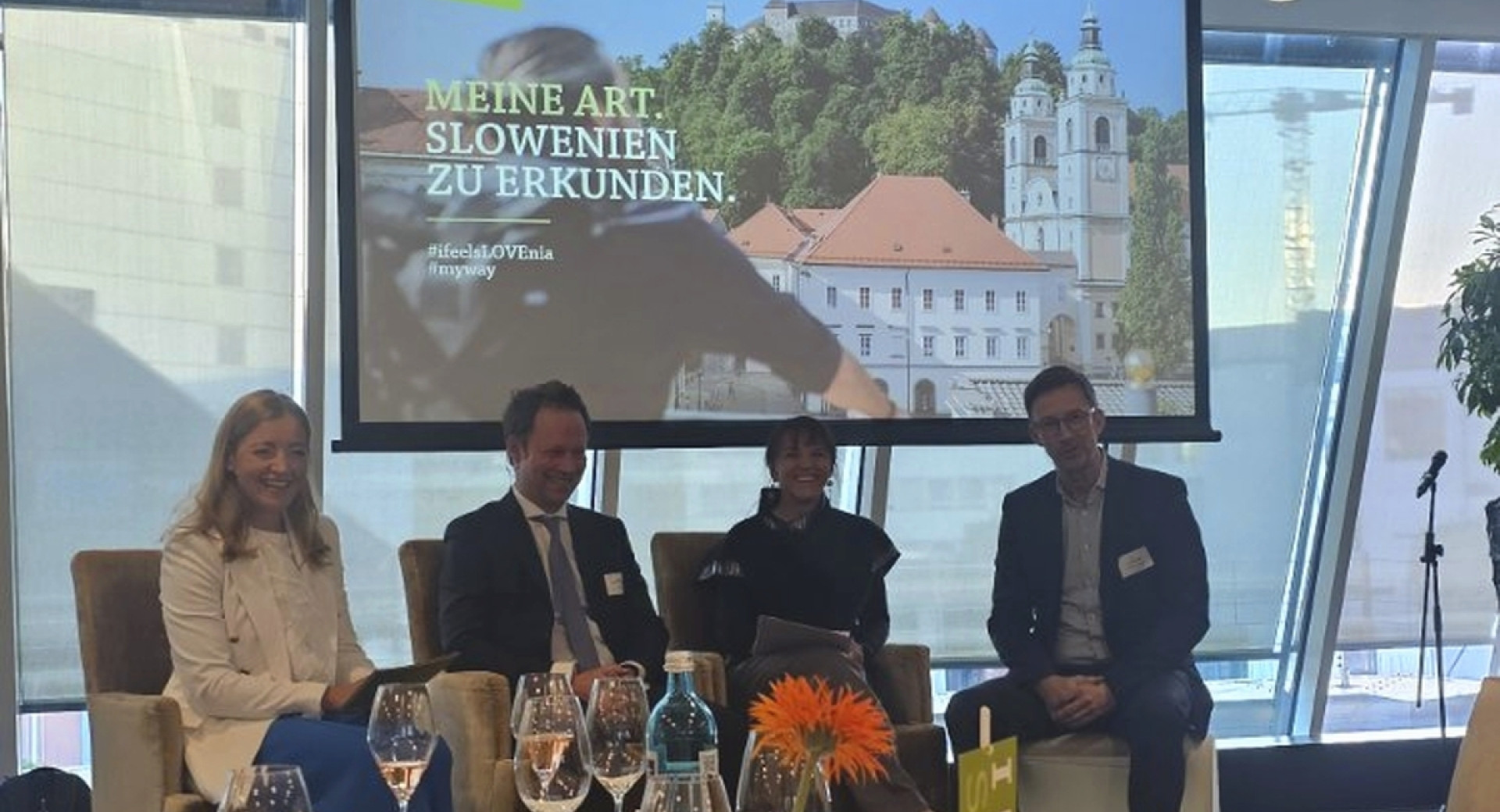 Štiri osebe sedijo pred večjim zaslonom s fotografijo Ljubljanskega gradu.