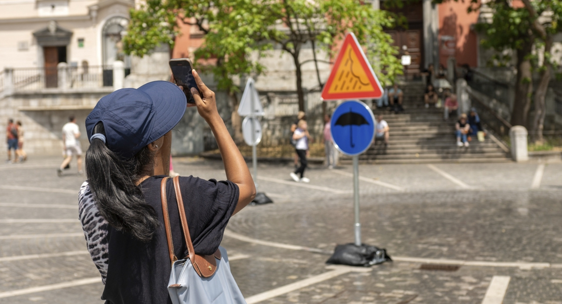 Oseba fotografira znaka z dežnikom in oblakom z dežjem v mestu.