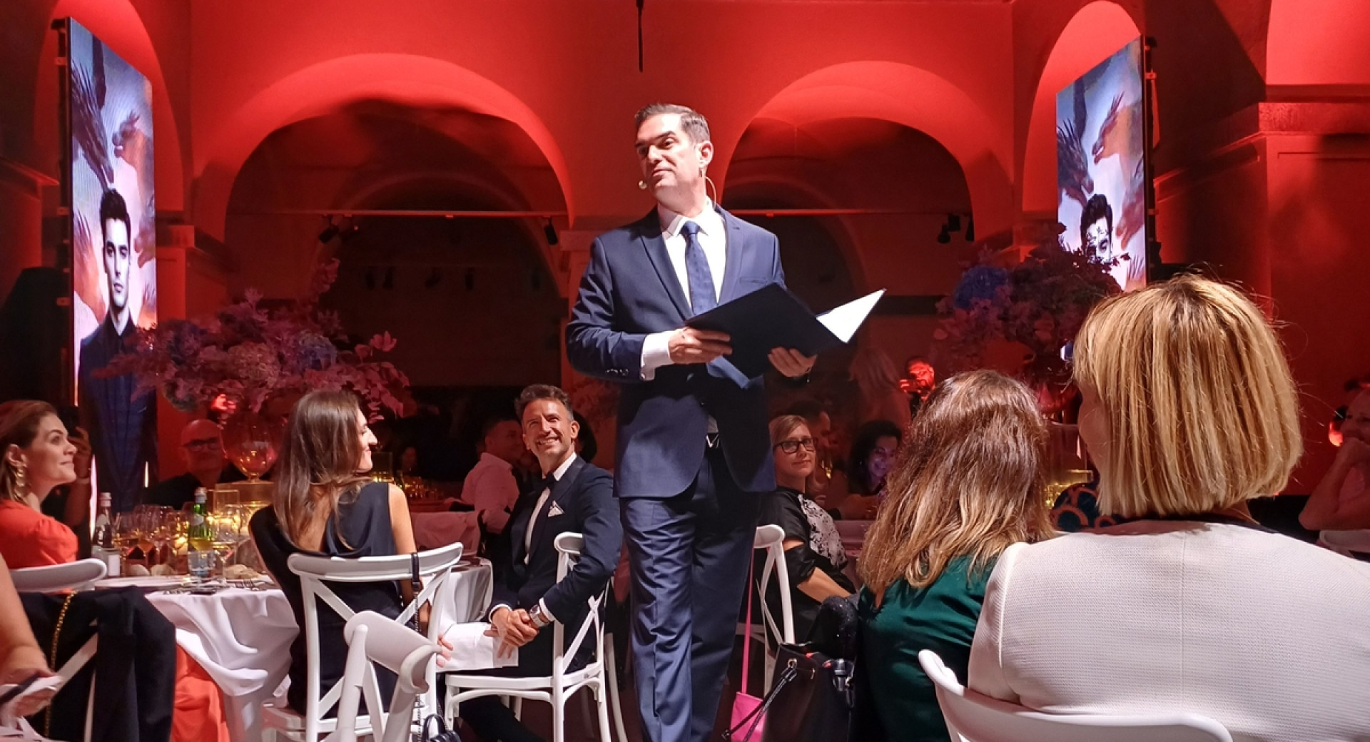 Slavnostna večerja z govorcem na manjšem privzdignjenem odru sredi prostora.