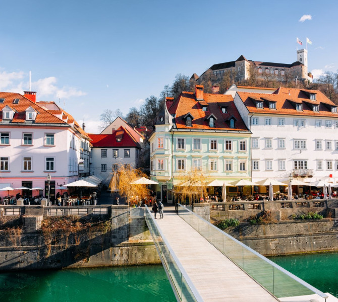 A glass bridge over the river, historic buildings, and a castle on the hill.