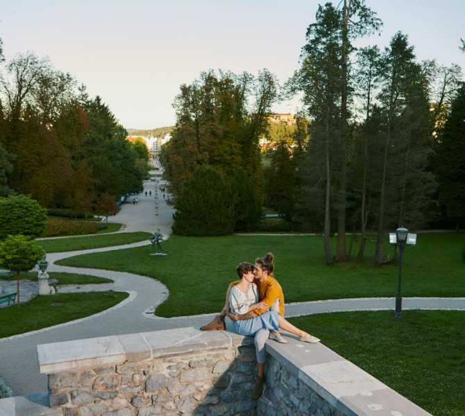 Zaljubljenca sedita na kamniti ograji, v ozadju pak. 