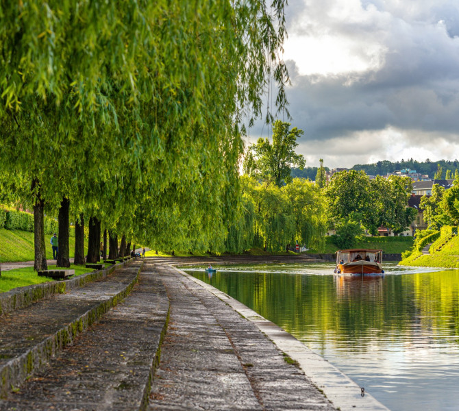 Ein Holzboot fährt auf dem Fluss, das Ufer voller Grün.