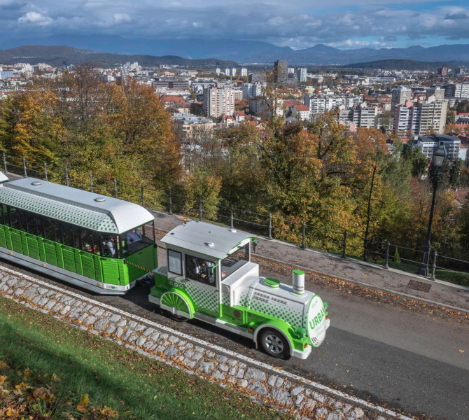 Un petit train touristique vert et blanc roulant sur la route avec la ville en arrière-plan.