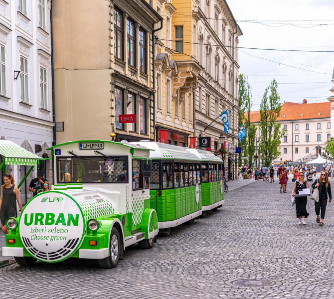 Petit train touristique vert et blanc dans la ville avec des gens à côté.