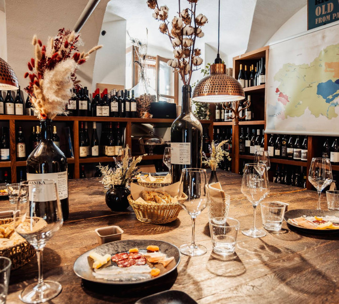 Weinflaschen, ein Weinglas und Teller mit Aufschnitt auf einem Holztisch.