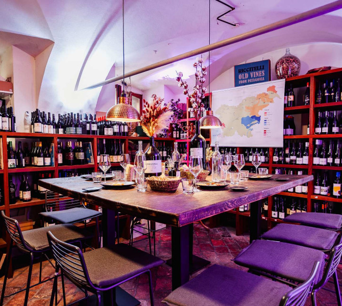 Ein Holztisch mit Stühlen, umgeben von Schränken und Regalen mit verschiedenen Weinsorten.