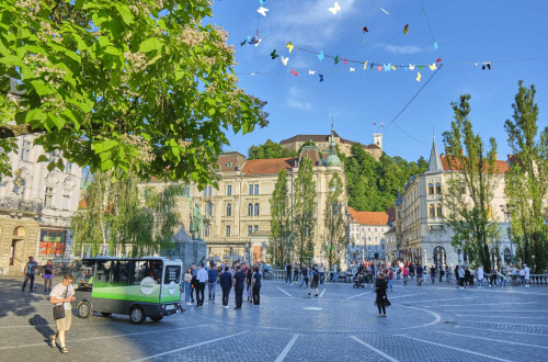 A city square surrounded by buildings, with a castle on the hill.