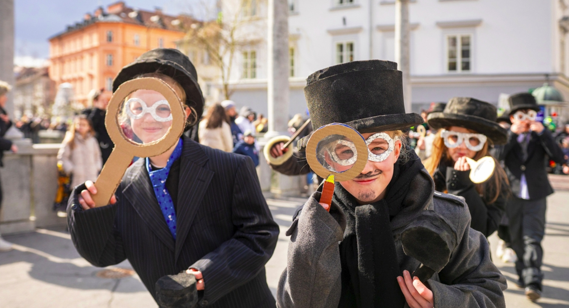 Pustni maski: otroka s cilindroma in povečevalnima stekloma pred obrazoma.