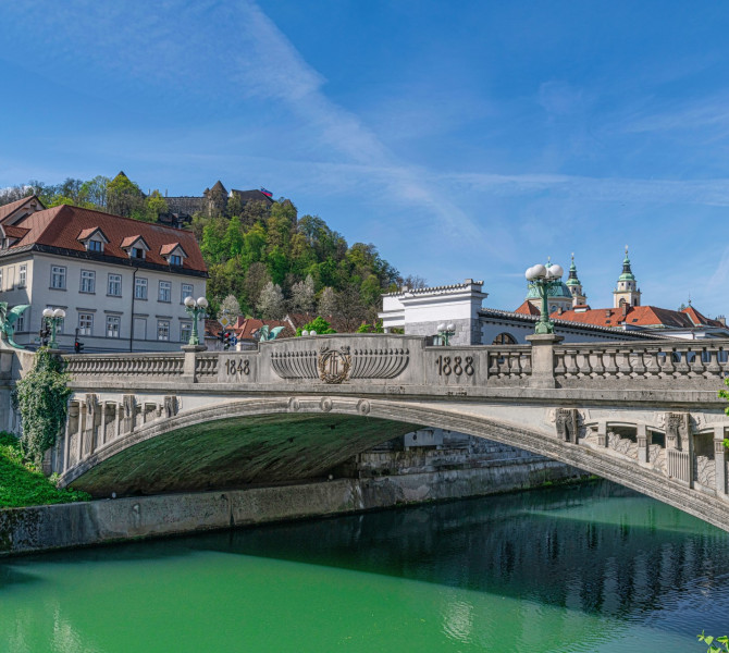 Most s kipi zmaja cez reko, v ozadju mescanske hise in grad nad mestom.