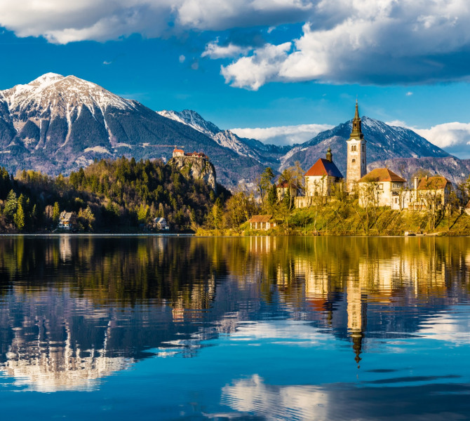 An island with a church on the lake, snow-capped mountains in the background.
